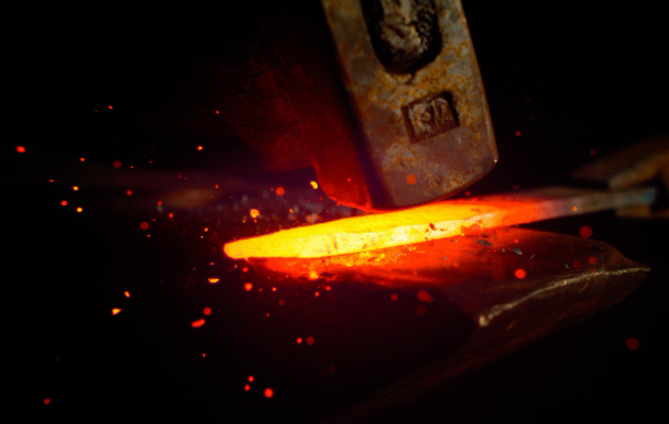 Molten steel being hand hammered onto an anvil as the smith creates a knife.