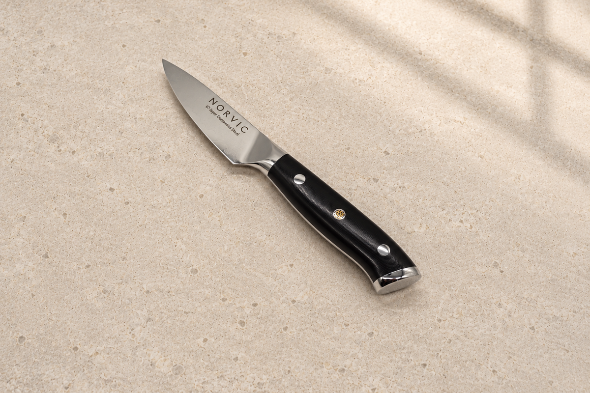 Norvic Worstead 3.5-inch paring knife, diagonal view on limestone with Damascus blade and black G10 handle