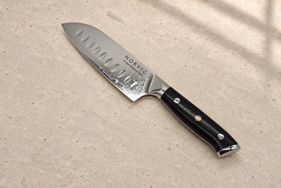 Norvic Worstead 5-inch santoku knife, diagonal view on limestone with Damascus blade and black G10 handle