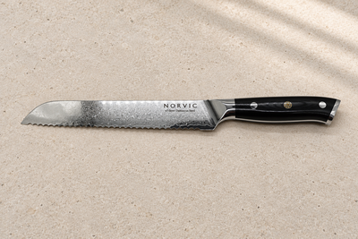 Side profile of the Norvic Worstead 8-inch bread knife, showing its serrated Damascus blade and black G10 handle