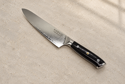 Norvic Worstead 8-inch chef knife, diagonal view on limestone with Damascus blade and black G10 handle